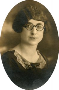 Portrait of the subject of the article In this sepia-toned head-and-shoulders portrait, Clara wears round glasses, bobbed and finger-waved hair with bangs, and a dress or blouse with a lace collar and a bow at the neckline.  She looks into the camera and, though she looks pleasant, she isn't smiling.